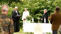 Drei Geistliche stehen hinter einem Altar, einer von ihnen liest einen Urkundentext vor.