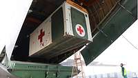 Ein Container mit einem roten Kreuz wird mit einem Hebekran aus der Maschine gehoben