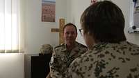 Der Pfarrer sitzt in seinem Büro und spricht mit einer Soldatin, die ihm gegenüber sitzt