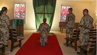 In der Kirche kniet der Militärpfarrer auf einem roten Teppich und blickt zum zentral in der Kirche stehenden Kreuz