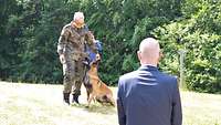 Ein zivil gekleideter Mann schaut sich einen Soldaten an, der einen Hund ausbildet.