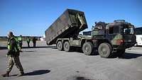 Ein Container auf einem Bundeswehr-Lkw wird durch einen Soldaten auf das Rollfeld des Flughafens abgelassen