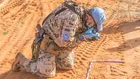 Ein Soldat kniet im Wüstensand und fotografiert einen Fußabdruck im Sand