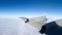 Der Tragflügel eines Flugzeugs samt Propeller hoch über den Wolken