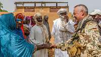 Soldat gibt einer malischen Frau die Hand, drumherum weitere Personen