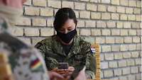 Eine kroatische Soldatin mit Mund-Nasen-Schutz sitzt an einem Tisch und blickt auf ihr Smartphone
