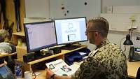 Ein Soldat sitzt im Büro an einem Schreibtisch und arbeitet am Computer