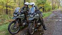 Zwei Soldaten sitzen auf einem Waldweg auf ihren Motorrädern und besprechen sich.