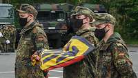 Zwei Soldaten und eine Soldatin stehen nebeneinander. Die Soldatin hält die Bundesdienstflagge in ihren Händen. 