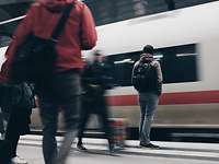 Mehrere Personen stehen auf dem Bahnsteig, während ein Zug einfährt