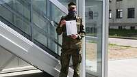 Ein Soldat steht mit einem Blatt Papier vor einem Gebäude