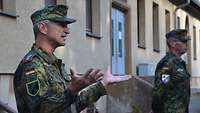 Soldat im Feldanzug steht vor einem Gebäude und gestikuliert beim Sprechen.