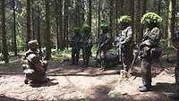 Mehrere Soldatinnen und Soldaten im Gefechtsanzug mit Tarnung stehen im Wald