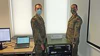 Zwei Soldaten mit Mund-Nasenschutz tragen zusammen einen Server bei der Übung CWIX.