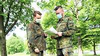 Feldwebel Jannis Siemer (li) und Hauptgefreiter Mats#de Staufenbiel (re) betrachten auf einer Wiese ein Dokument