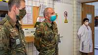 Zwei Soldaten im Feldanzug und eine Zivilistin im weißen Kittel stehen in einem Labor.