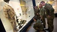 Soldaten der Bundeswehr stehen und hocken vor einem Schaukasten mit Exponaten in einem Museum.