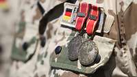 Zwei Einsatzmedaillen der Bundeswehr in Bronze sind an einem Feldanzug angesteckt.