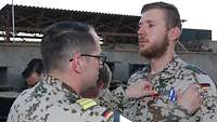 Ein Soldat befestigt die Einsatzmedaille der Bundeswehr an der Uniformjacke eines Soldaten.