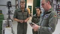Ein Ausbilder der Bundeswehr spricht mit zwei jungen Auszubildenden vor einer Maschine in einer Werkstatt