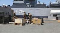 Zwei Soldaten vor der Korvette „Ludwigshafen am Rhein“, vor ihnen Kisten, links ein Container