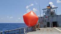 Soldaten auf dem Flugdeck einer Korvette lassen einen großen roten Luftsack als Übungsziel zu Wasser