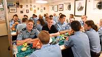 Soldatinnen und Soldaten sitzen in blauer Arbeitsuniform zusammen an Tischen beim Essen.