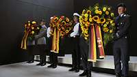 Bundeswehrsoldaten stehen im Raum der Stille und halten Blumenkränze.