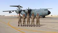 Fünf Soldaten stehen auf einem Rollfeld in Reihe, im Hintergrund steht quer ein Airbus A400M