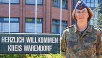 Halbporträt einer Soldatin vor dem Schild des Kreishauses Warendorf