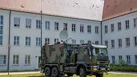 Ein Militär-LKW mit drei verschiedenen Antennenaufbauten steht vor einem weißen Gebäude.