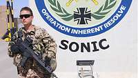 Eine Soldatin steht bewaffnet vor einer Betonstehle, auf der das Wappen der Operation Inherent Resolve zu sehen ist