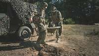 Zwei Soldaten tragen den Bauteil eines Mörsers aus einem Geländewagen. 