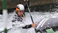 Junger Mann paddelt beim Kanuslalom. Wasser spritzt ihm ins Gesicht.