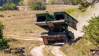 Ein Panzer mit einer verlegefähigen Brücke fährt durch das Gelände