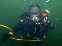 Eine Person im Tauchanzug unter Wasser blickt direkt in die Kammera.