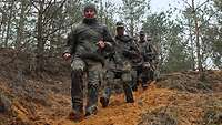 Fünf Soldaten laufen auf einem sandigen, schmalen Pfad einen Berg hinunter. 