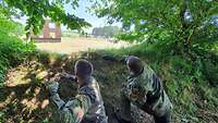 Soldaten werfen Übungshandgranaten auf eine ferne Hausattrappe, in der Schützenscheiben sind.