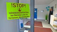 Ein Schild mit der Aufschrift Stop Händedesinfektion bei Betreten und vor Verlassen des Gebäudes