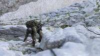 Mit Rucksack und Gewehr klettert ein Soldat der Gebirgstruppe eine steile Felswand hinauf.