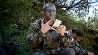 Ein Soldat nutzt Tarnschminke im Gesicht, um sich an die Farbe der Umgebung anzupassen. 