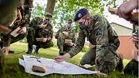 Auf einer Wiese knien Soldaten im Halbkreis um einen Kameraden, der etwas in eine Karte zeichnet.