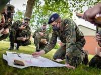 Auf einer Wiese knien Soldaten im Halbkreis um einen Kameraden, der etwas in eine Karte zeichnet.