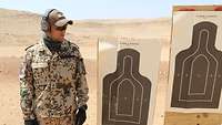 Ein Soldat steht in der Wüste neben zwei Zielscheiben und betrachtet sein Schießergebnis