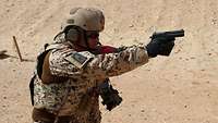 Ein Soldat in der Wüste hält eine Handfeuerwaffe und zielt mit gestreckten Armen