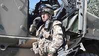 Ein Soldat steht neben der geöffneten Tür eines Militärfahrzeuges und telefoniert..