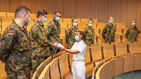 Eine Frau überreicht weiße Kleidung an einem Soldaten im Feldanzug.