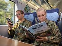 Soldatin sitzt neben ihrem Kameraden im Zug und liest eine Zeitung.