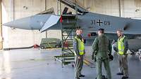 Zwei Techniker besprechen vor dem Flugzeug in einer Halle mit dem Piloten, ob es technische Probleme am Eurofighter gab.