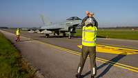 Ein Techniker gibt einem Piloten im Eurofighter mit gekreuzten Armen das Signal, auf der Rollbahn zu halten.